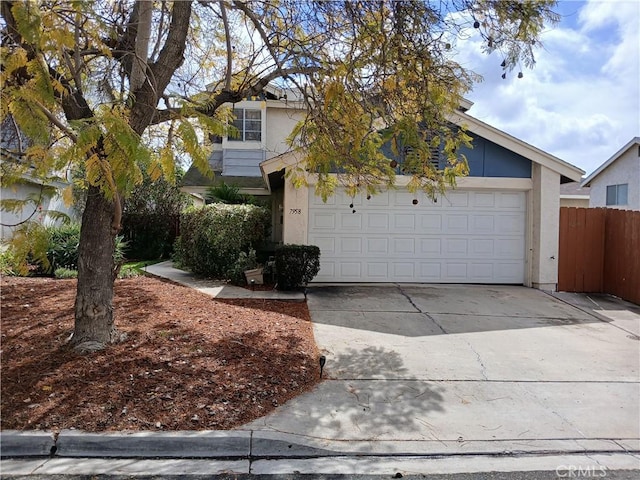 view of property hidden behind natural elements with driveway, stucco siding, and fence