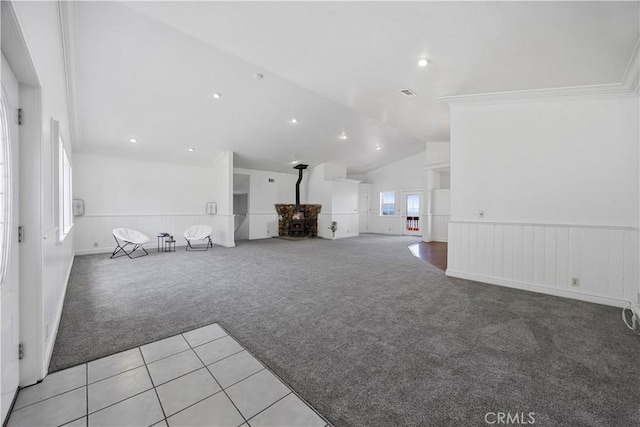 unfurnished living room featuring light colored carpet, a wainscoted wall, vaulted ceiling, ornamental molding, and light tile patterned floors