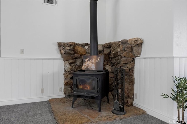 detailed view of a wood stove, carpet, a wainscoted wall, and a decorative wall