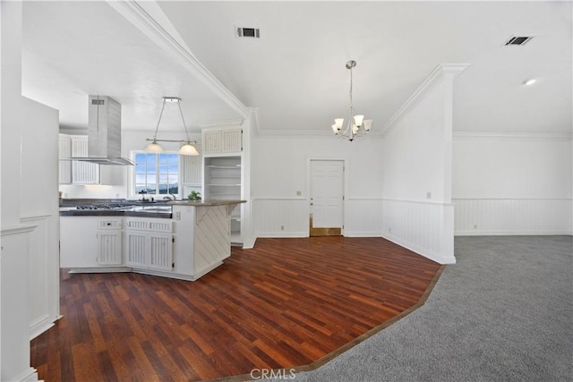 kitchen with island exhaust hood, a chandelier, dark countertops, white cabinets, and wainscoting