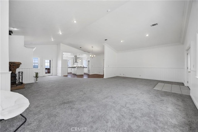 unfurnished living room featuring carpet flooring, a stone fireplace, wainscoting, a decorative wall, and vaulted ceiling