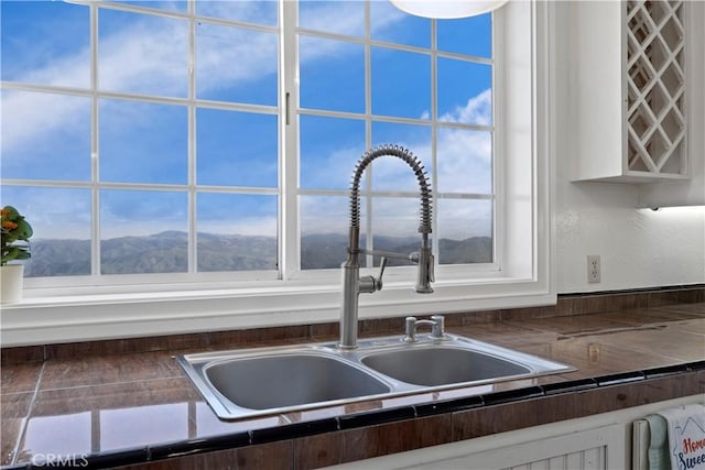 kitchen view of a sink, white cabinetry, dark countertops, and a mountain view