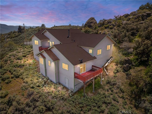 back of property at dusk with a balcony and roof with shingles