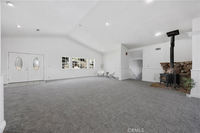 unfurnished living room featuring carpet flooring, a wood stove, lofted ceiling, wainscoting, and recessed lighting