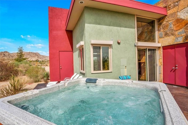 rear view of property with a hot tub, a mountain view, stucco siding, and stone siding