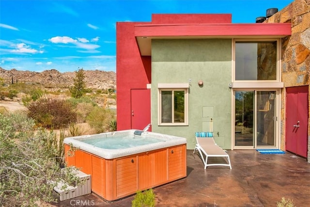 back of house featuring a hot tub, a patio area, stucco siding, and a mountain view