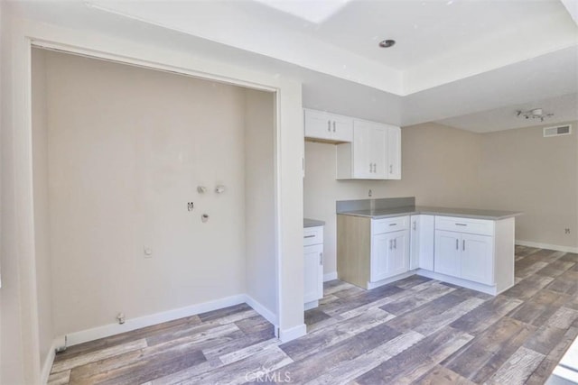kitchen featuring light wood-style floors, white cabinetry, baseboards, a peninsula, and a raised ceiling