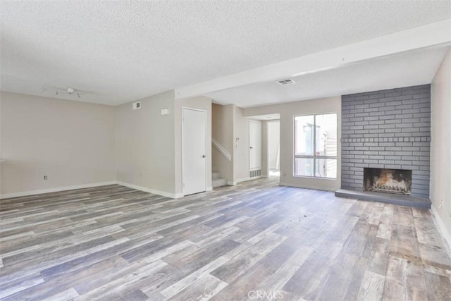 unfurnished living room featuring a textured ceiling, wood finished floors, stairs, a fireplace, and baseboards