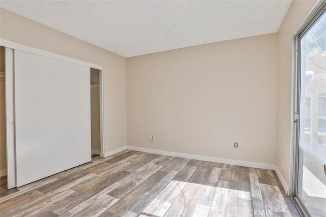 unfurnished bedroom with a textured ceiling, wood finished floors, a closet, baseboards, and access to outside