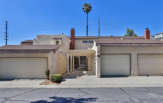 townhome / multi-family property featuring a pergola, a shingled roof, a chimney, and community garages