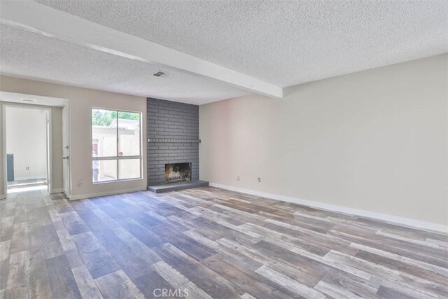 unfurnished living room featuring a textured ceiling, wood finished floors, a fireplace, and baseboards