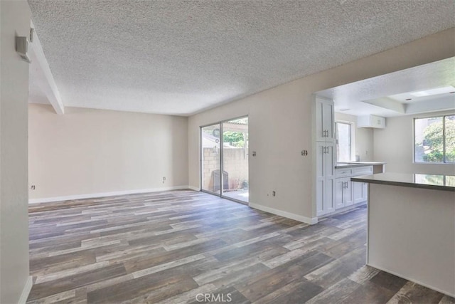 unfurnished living room with wood finished floors, a textured ceiling, and baseboards
