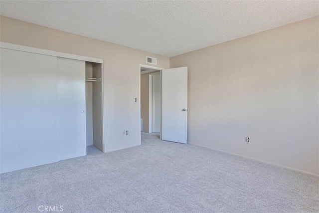 unfurnished bedroom with light carpet, a textured ceiling, and a closet