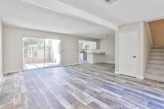 unfurnished living room featuring light wood finished floors, stairway, a textured ceiling, and baseboards