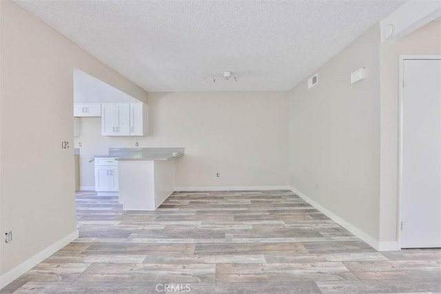 unfurnished living room featuring a textured ceiling, light wood-style flooring, baseboards, and rail lighting