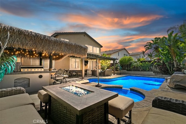 pool at dusk featuring a fire pit, a patio, an outdoor kitchen, and a pool with connected hot tub