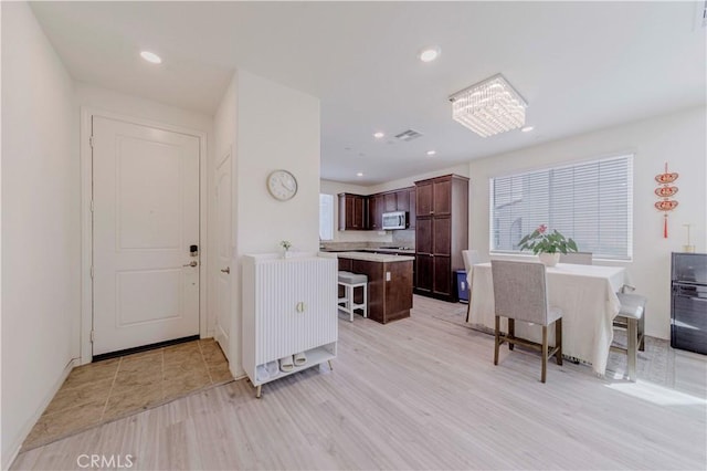 14533 Verona Pl, Eastvale, CA 92880 - kitchen with stainless steel microwave, a kitchen bar, dark brown cabinets, light countertops, and light wood-style floors
