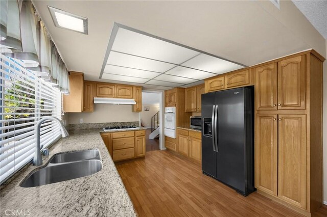 9906 Cedar Ct, Cypress, CA 90630 - kitchen with black fridge with ice dispenser, a sink, stainless steel microwave, under cabinet range hood, and white oven