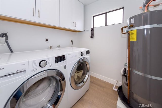 laundry area with strapped water heater, washer and clothes dryer, cabinet space, light wood finished floors, and baseboards