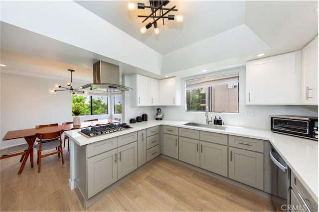kitchen featuring a chandelier, stainless steel appliances, a sink, wall chimney range hood, and gray cabinets