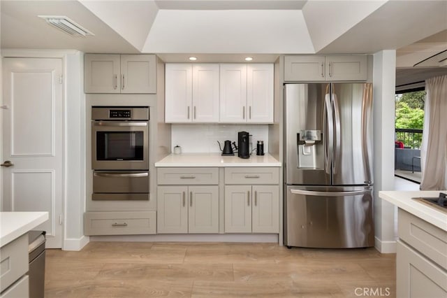 kitchen with stainless steel appliances, a warming drawer, gray cabinetry, light countertops, and light wood-type flooring