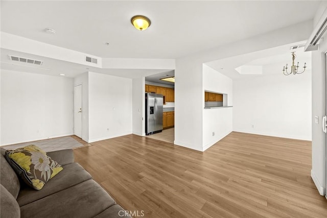 unfurnished living room with baseboards, a chandelier, and light wood finished floors