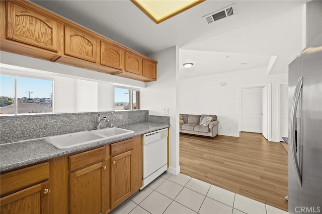 kitchen featuring a sink, white dishwasher, freestanding refrigerator, light tile patterned floors, and brown cabinets