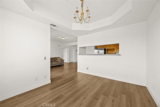 unfurnished living room with a chandelier, a raised ceiling, baseboards, and wood finished floors
