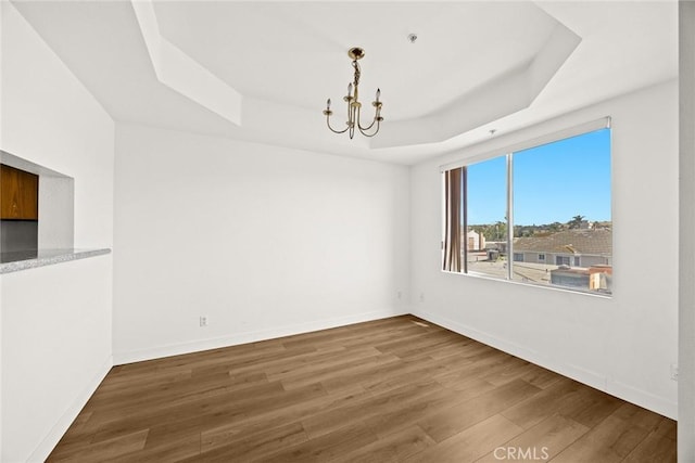 empty room with a tray ceiling, a chandelier, wood finished floors, and baseboards