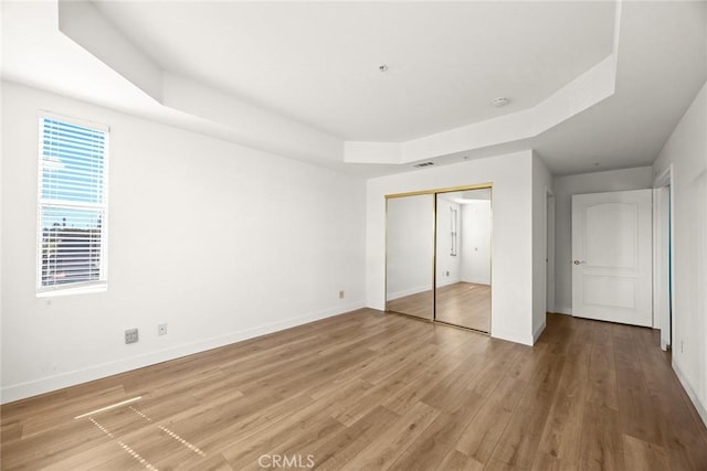 unfurnished bedroom with baseboards, light wood-type flooring, a closet, and a raised ceiling