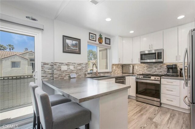 37 Fleurance St, Laguna Niguel, CA 92677 - kitchen with appliances with stainless steel finishes, a peninsula, white cabinetry, light wood-style floors, and decorative backsplash