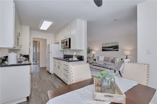 kitchen with stainless steel microwave, dark countertops, freestanding refrigerator, and white cabinetry