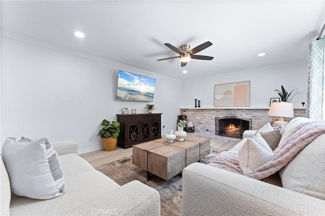 living area featuring ceiling fan, a brick fireplace, wood finished floors, ornamental molding, and recessed lighting