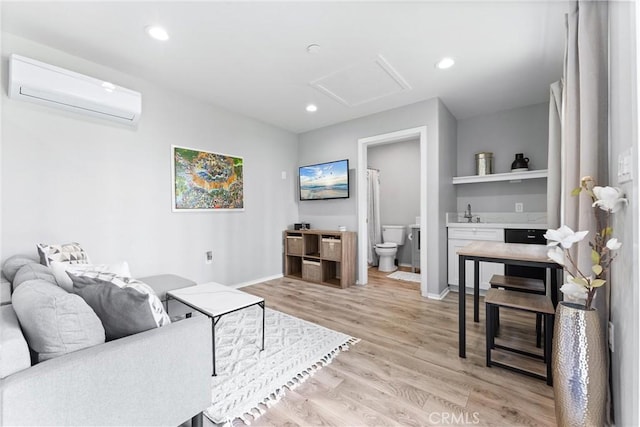 living area with a wall unit AC, attic access, light wood-type flooring, baseboards, and recessed lighting