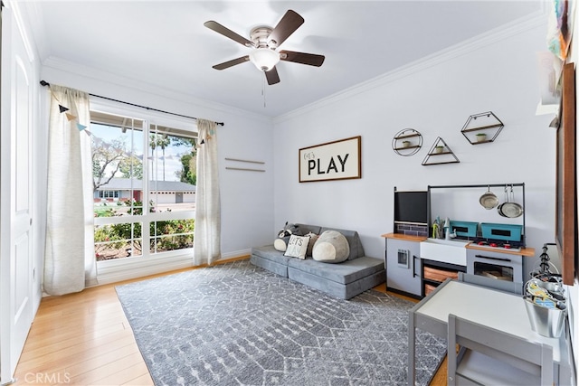living area with wood finished floors, ornamental molding, and a ceiling fan