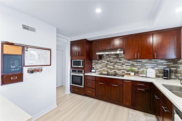 kitchen with stainless steel appliances, under cabinet range hood, backsplash, and light wood-type flooring