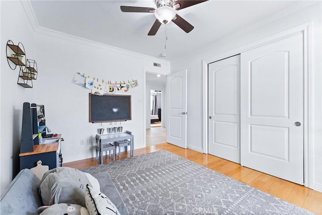 bedroom with ornamental molding, wood finished floors, a ceiling fan, a closet, and baseboards