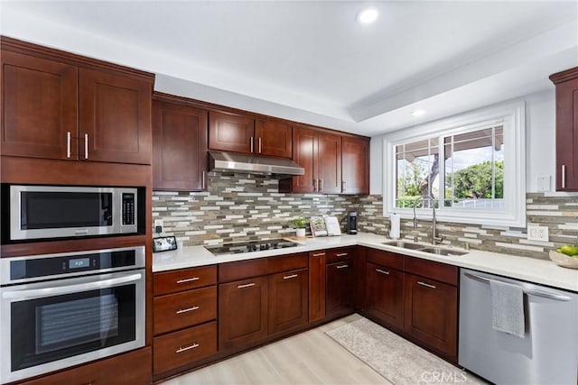 kitchen with appliances with stainless steel finishes, a sink, under cabinet range hood, light countertops, and recessed lighting