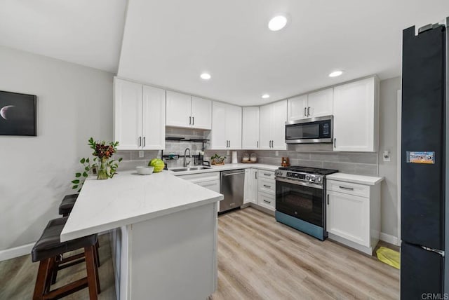 kitchen with appliances with stainless steel finishes, a peninsula, a sink, white cabinetry, and decorative backsplash