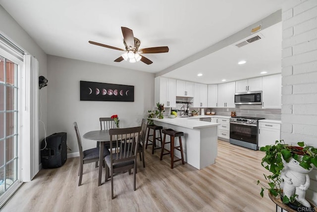 kitchen featuring stainless steel appliances, a peninsula, white cabinetry, decorative backsplash, and light countertops