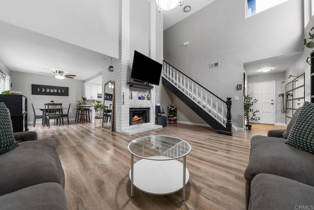 living room featuring a high ceiling, stairway, a fireplace, wood finished floors, and a ceiling fan