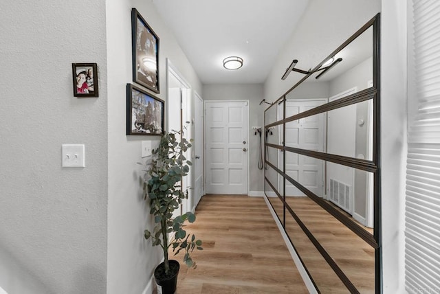 hall with light wood-style floors, a textured wall, and baseboards