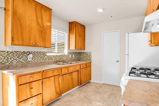 kitchen featuring a sink, light countertops, under cabinet range hood, and decorative backsplash