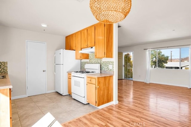 kitchen featuring white appliances, under cabinet range hood, a chandelier, and light countertops