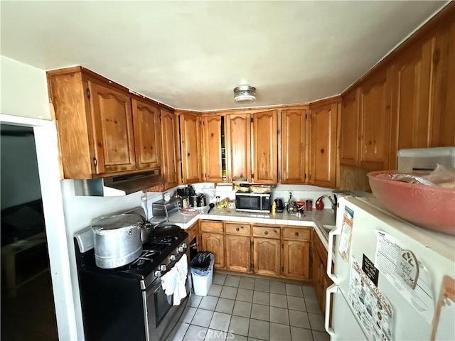 106 N Encina Ave, Rialto, CA 92376 - kitchen with refrigerator, light tile patterned floors, stainless steel range with gas stovetop, brown cabinetry, and tile counters