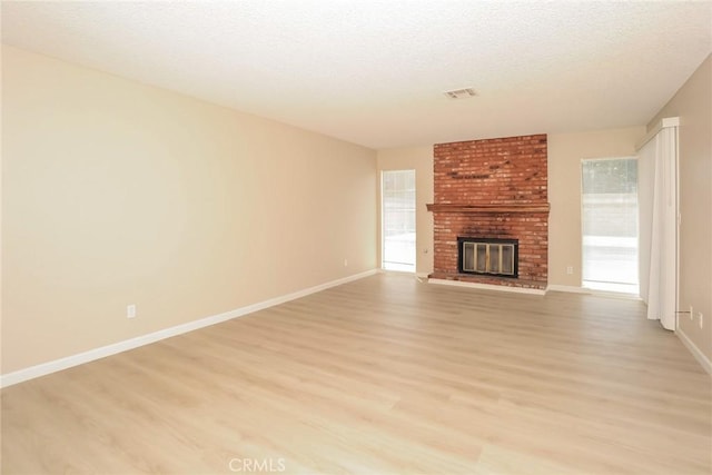 1536 Granicy Dr, Lancaster, CA 93535 - unfurnished living room featuring light wood finished floors, a brick fireplace, baseboards, and a textured ceiling