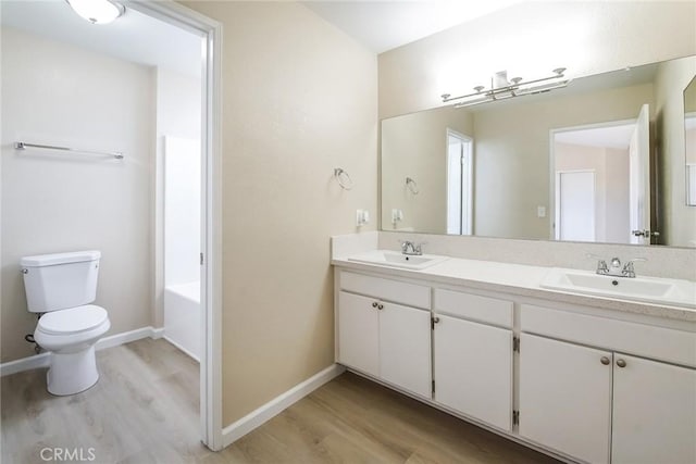 bathroom featuring wood finished floors, toilet, double vanity, and a tub