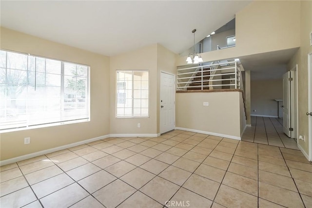 empty room with a chandelier, light tile patterned floors, baseboards, and high vaulted ceiling
