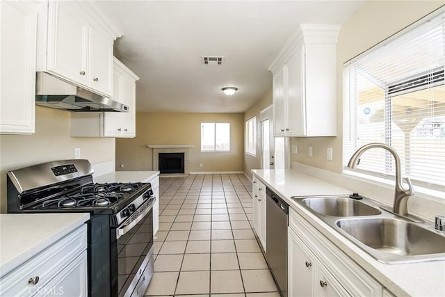 kitchen with appliances with stainless steel finishes, under cabinet range hood, a sink, open floor plan, and a brick fireplace
