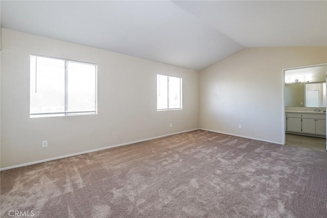 unfurnished bedroom featuring carpet floors, vaulted ceiling, baseboards, and ensuite bathroom